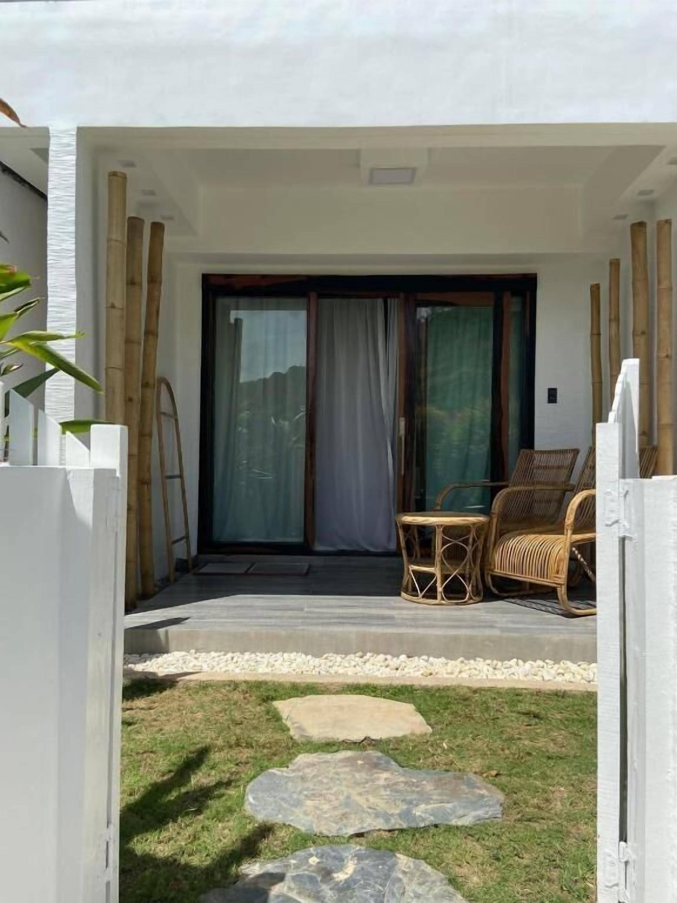 Une maison moderne dotée d’un patio couvert, d’une porte-fenêtre coulissante et d’un petit espace extérieur aménagé avec des meubles en osier.