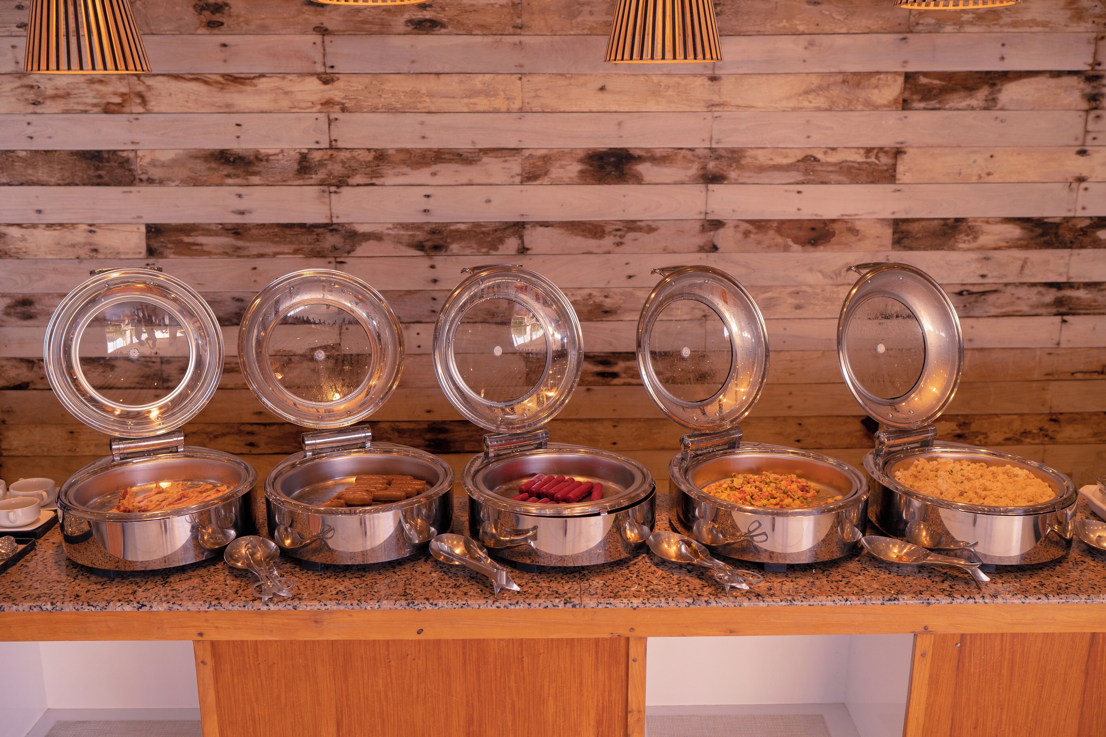 A buffet with multiple food containers, each with a lid, on a counter against a wooden wall.