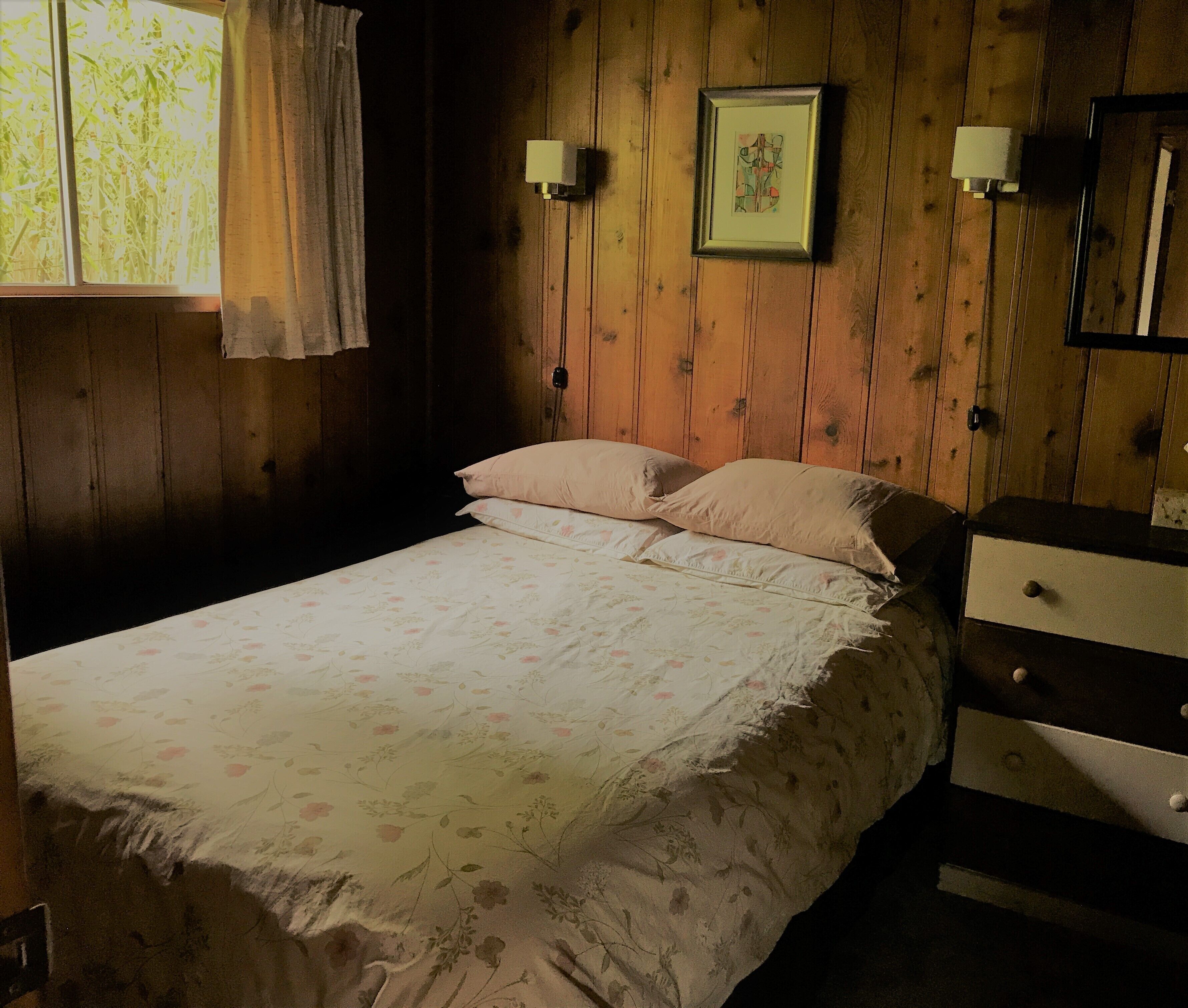 Una habitación con paneles de madera, una cama, un aparador y un cuadro en la pared.