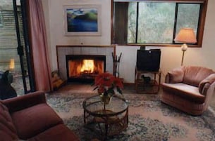 Uma sala de estar com lareira, um sofá, uma poltrona e um abajur.