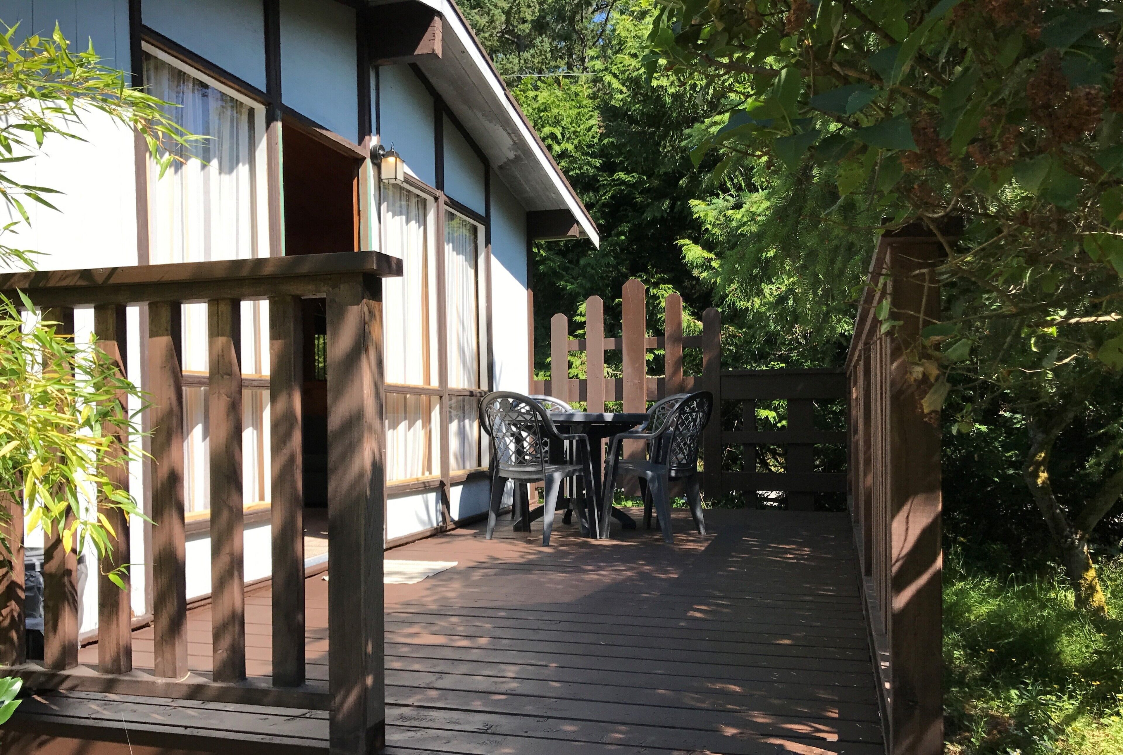 A wooden deck with a table and chairs, surrounded by a wooden fence and greenery.