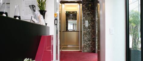 An elevator with a red carpet leading to a room with a marble wall and a clock on the wall.