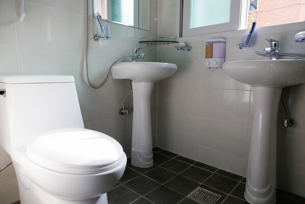 Un baño con inodoro, dos lavamanos y ducha.
