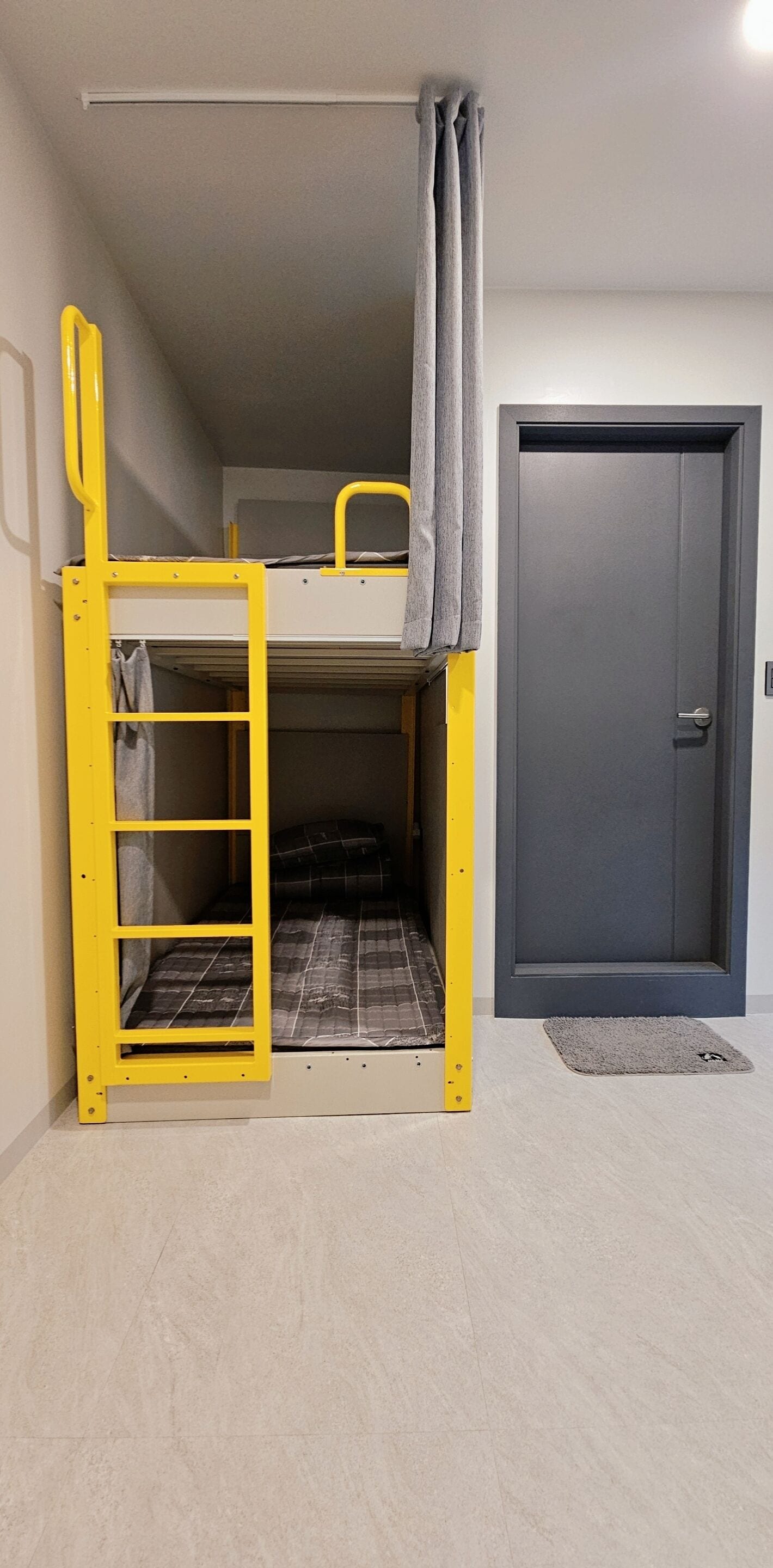 A bunk bed with a ladder, a door, and a small rug on the floor.