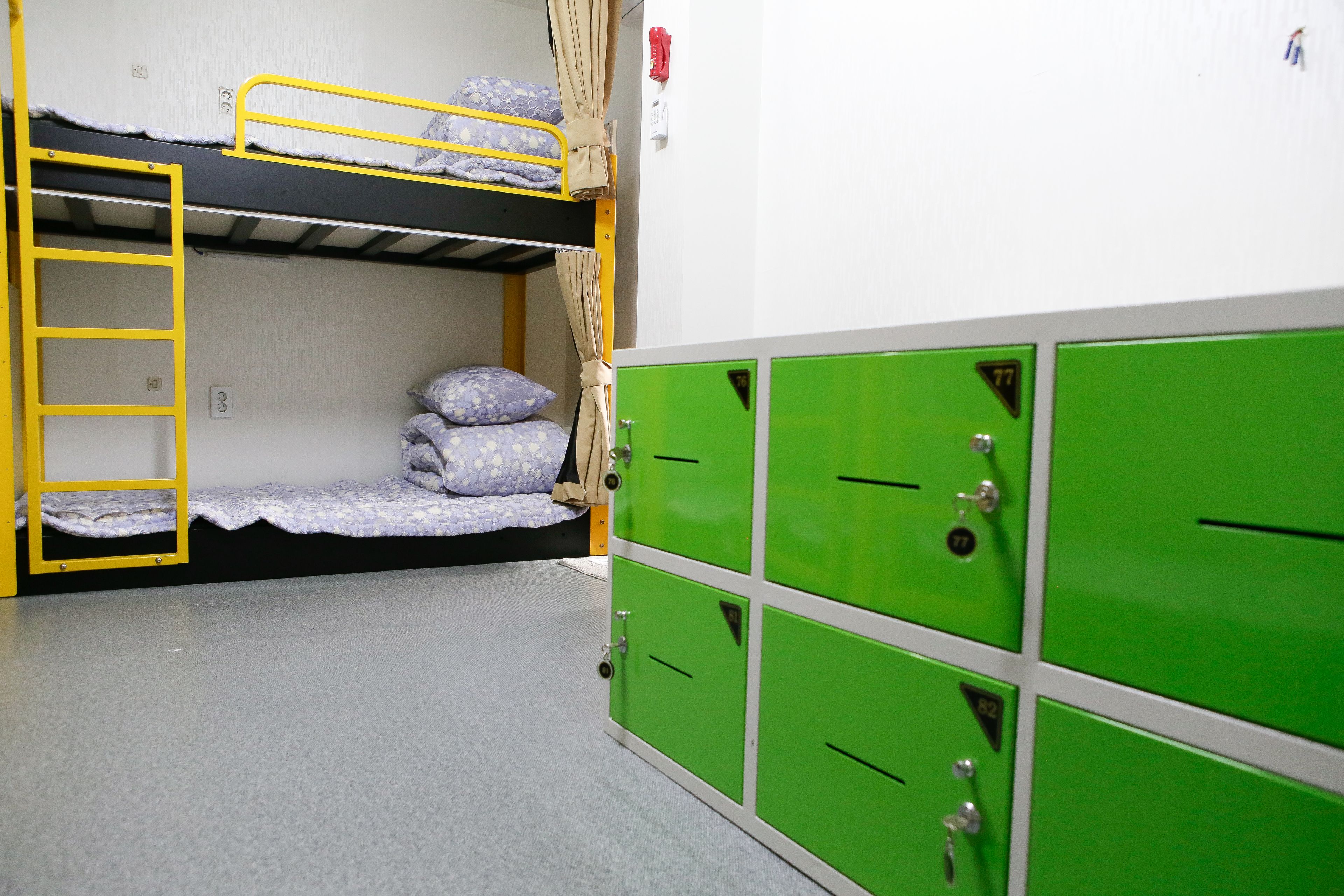 A bunk bed room with a ladder, a single bed with pillows, and green lockers.