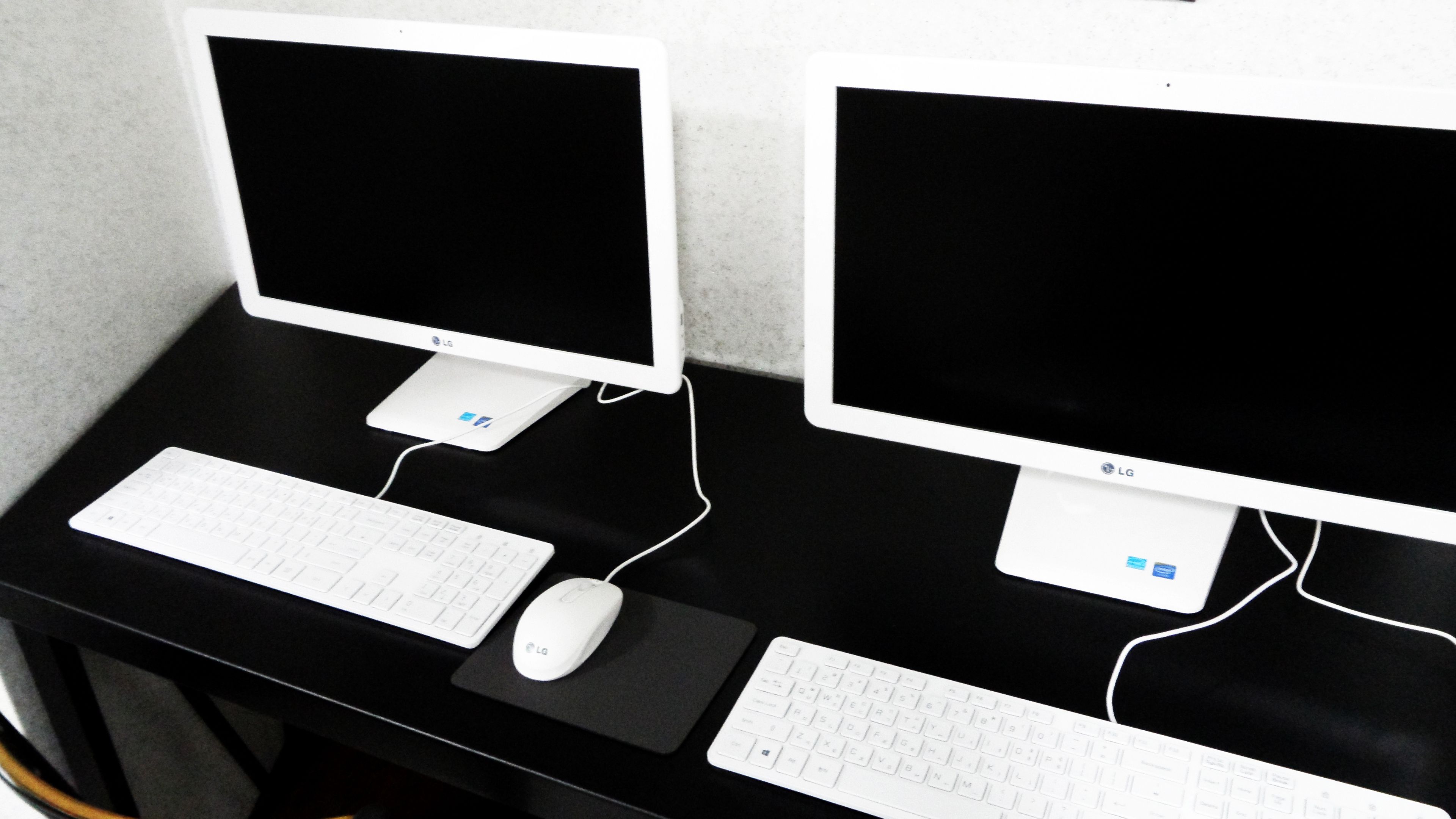 Dos monitores LG sobre un escritorio negro con teclados y ratón blancos.