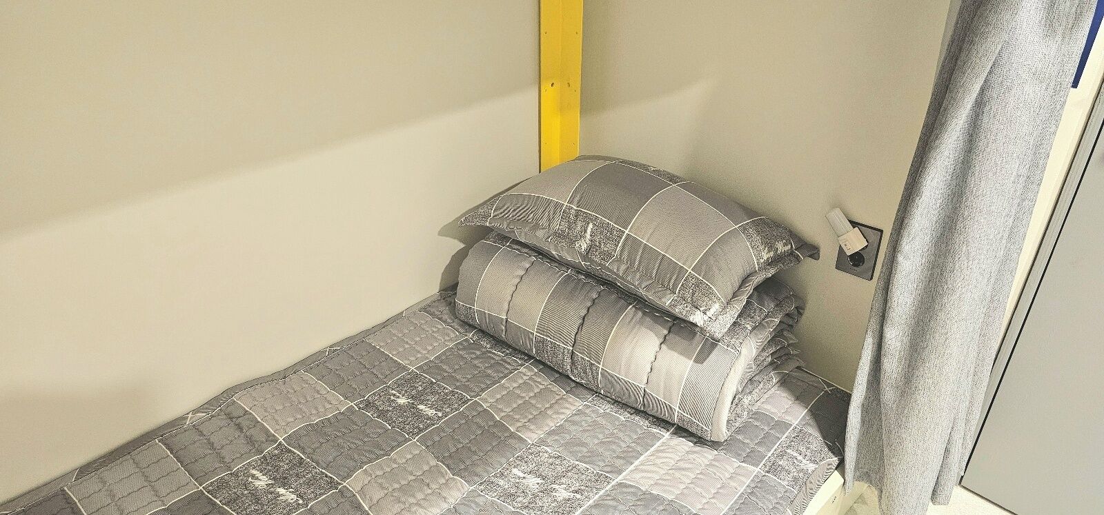Una habitación pequeña con una cama individual, colcha gris acolchada y almohadas a juego.
