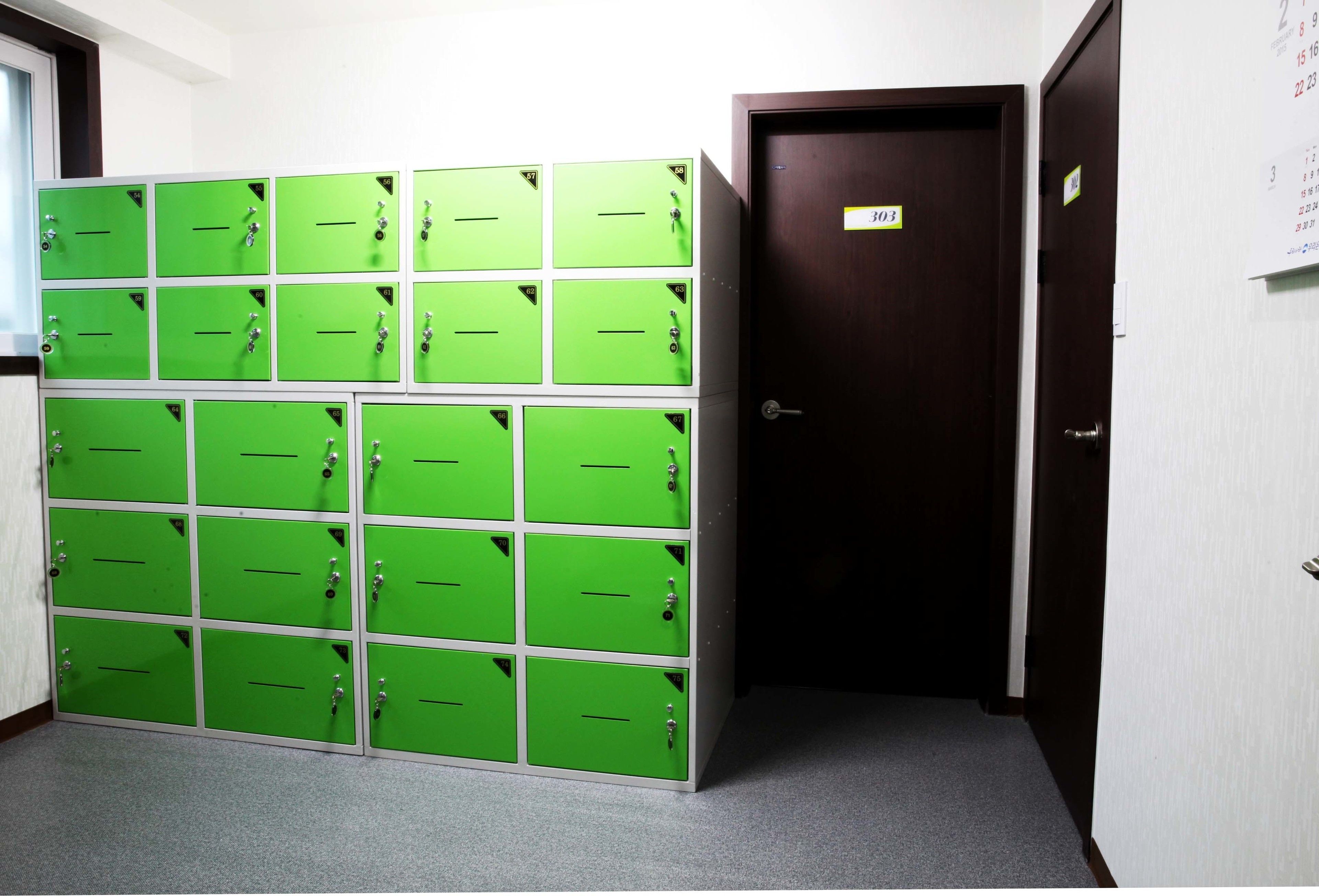 A row of green lockers in a hallway with a door labeled "303" and a calendar on the wall.