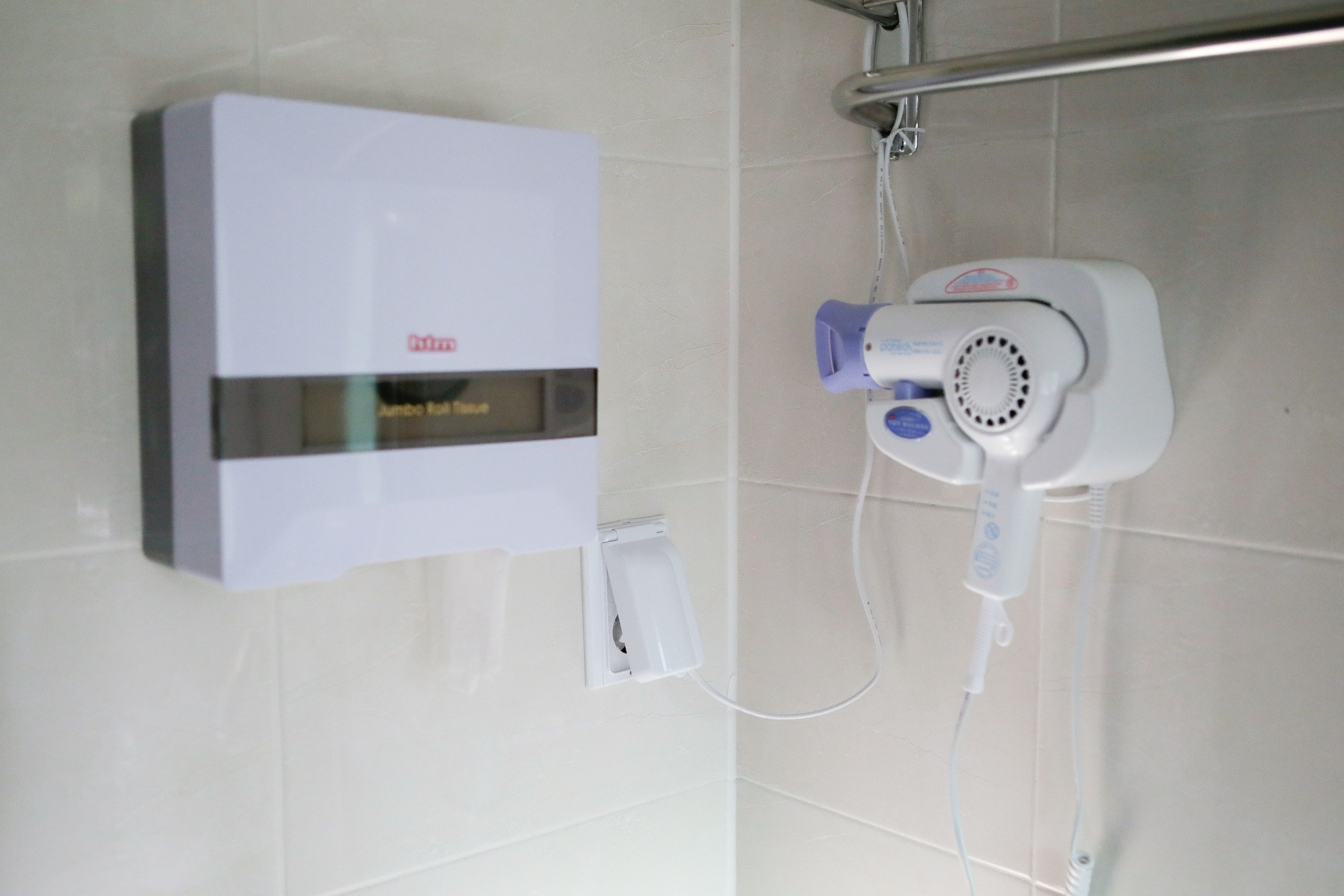 Une salle de bain avec un radiateur blanc fixé au mur, une douchette blanche et une prise électrique blanche.