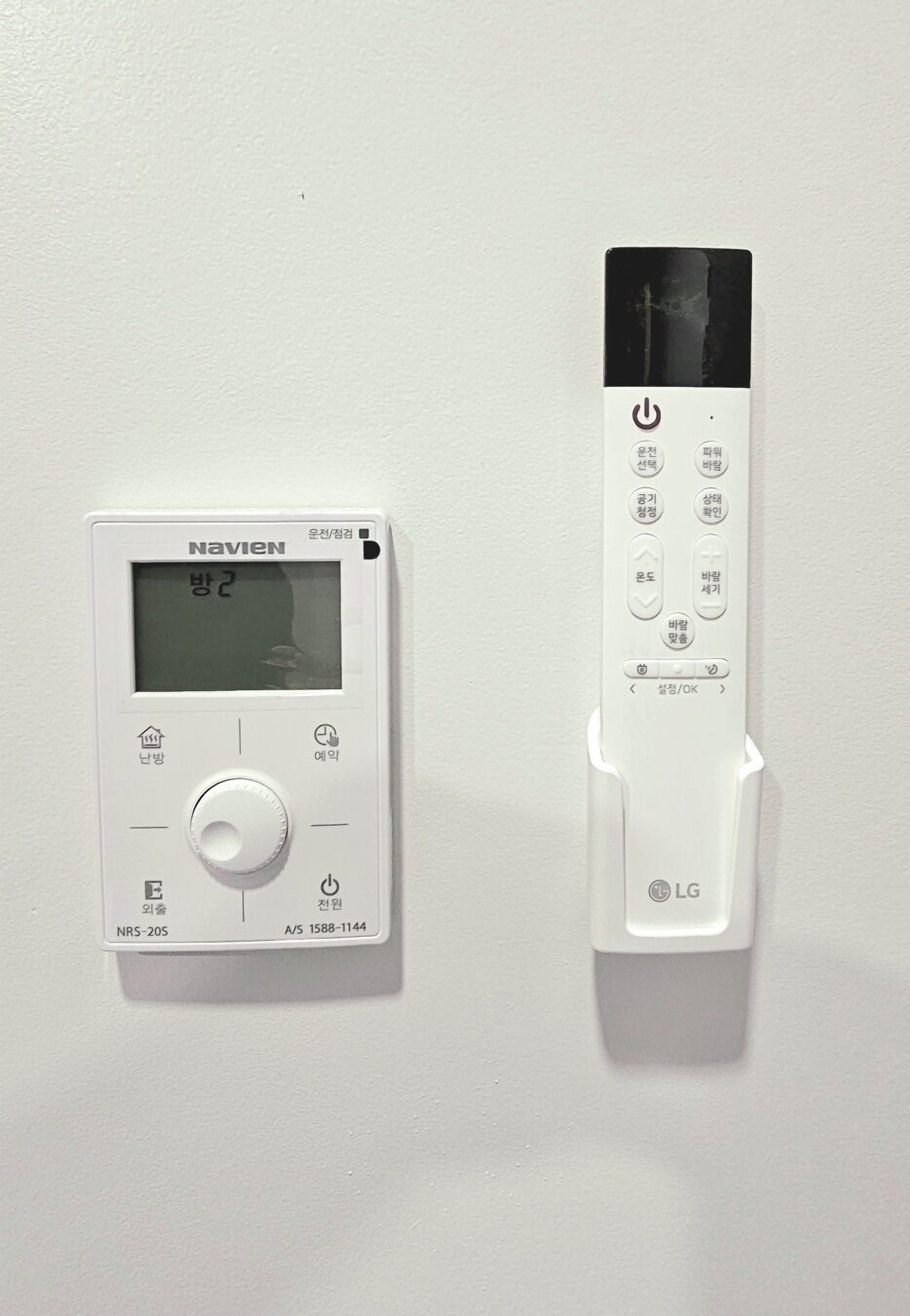 Two wall-mounted thermostats, one labeled Navien and the other LG, with control buttons and a display screen.