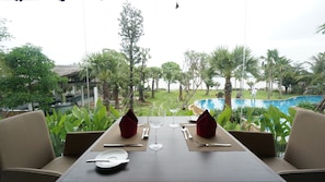 Mesa de comedor lista con cubiertos y copas de vino, con vista a una piscina y exuberante vegetación.