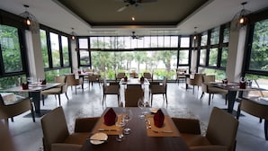 Un restaurante con varias mesas y sillas, amplias ventanas que dan a zonas verdes y ventiladores de techo.