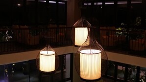 Un interior moderno con lámparas colgantes, barandilla de vidrio y una zona de estar con sillas.