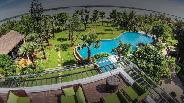 Zona de piscina con vista despejada al agua, rodeada de follaje y palmeras.