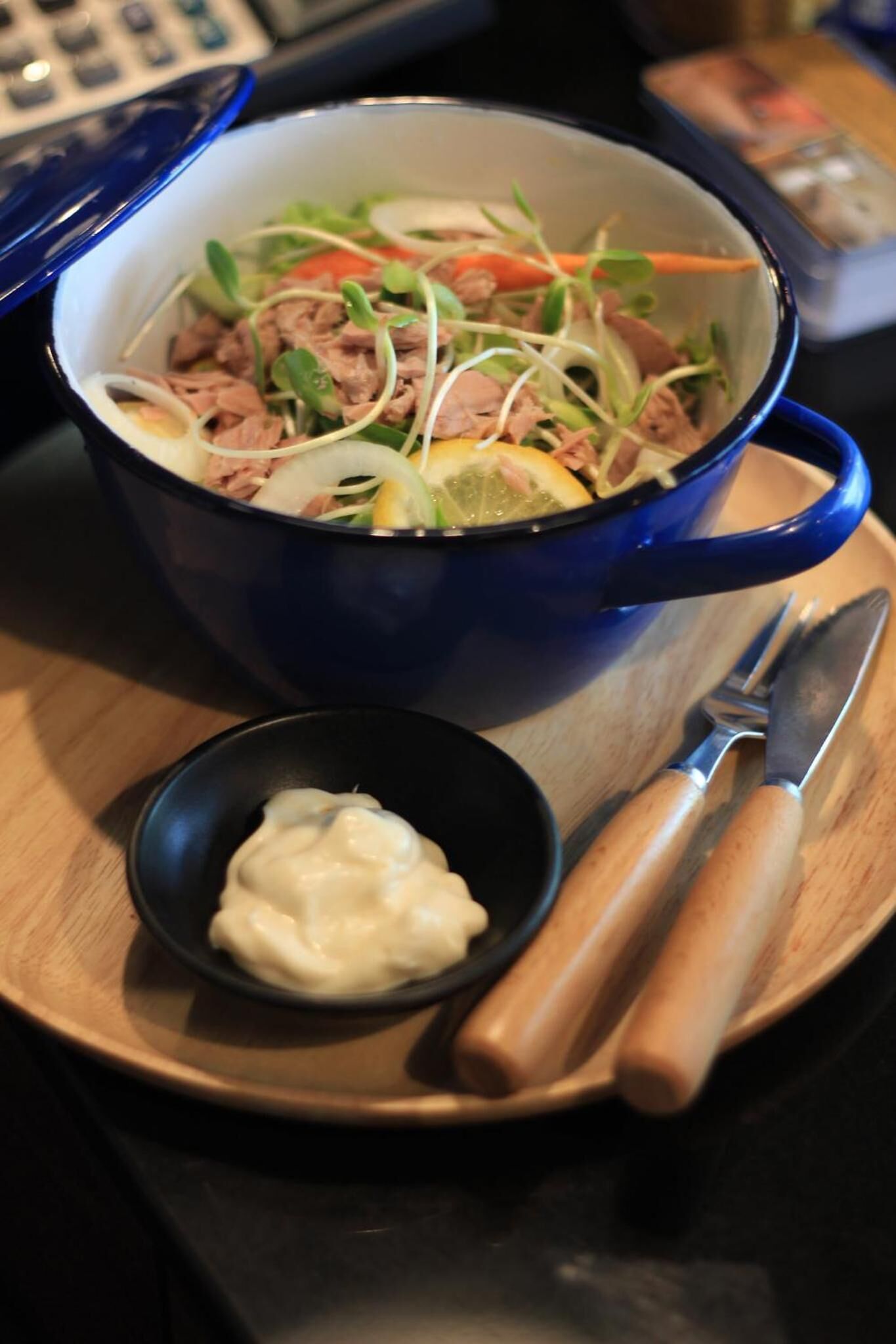 Un saladier bleu rempli de salade, accompagné d’un petit bol de vinaigrette et d’un couteau, le tout posé sur un plateau en bois.