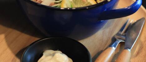 A blue bowl of salad with a small bowl of dressing and a knife on a wooden tray.