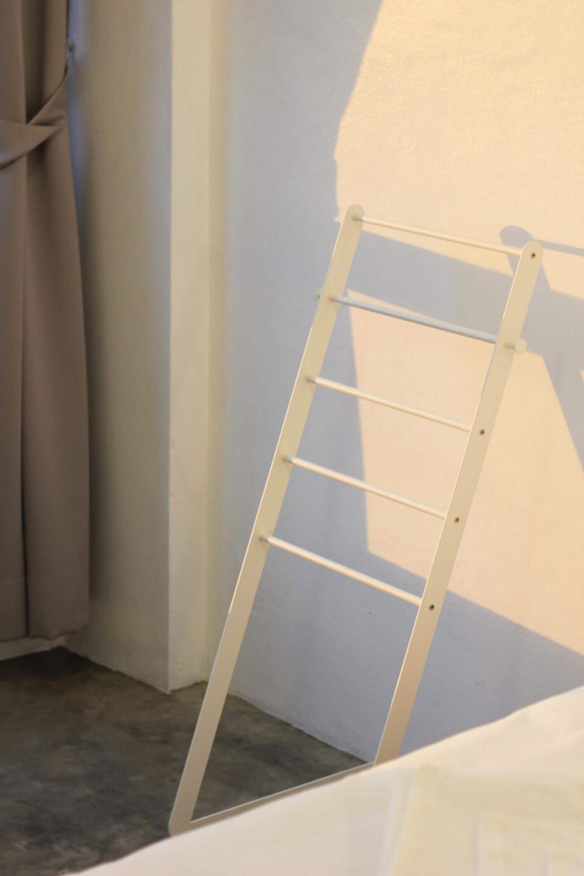 A white ladder leaning against a wall in a room with a plain, light-colored floor.