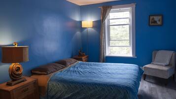 A bedroom with a bed, a nightstand, a lamp, a chair, and a window.