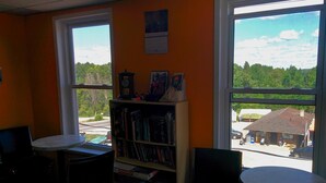 Een kamer met twee ronde tafels, een boekenkast en uitzicht op een weg en gebouwen.