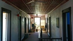 Een hal met een rood patroonplafond, een centrale trap en een deur naar een kamer met een bureau en stoel.