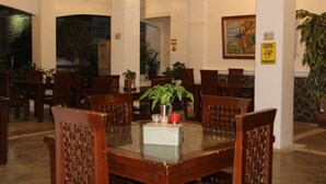 Un comedor con una mesa de vidrio rodeada de sillas de madera, plantas en macetas y un cuadro en la pared.