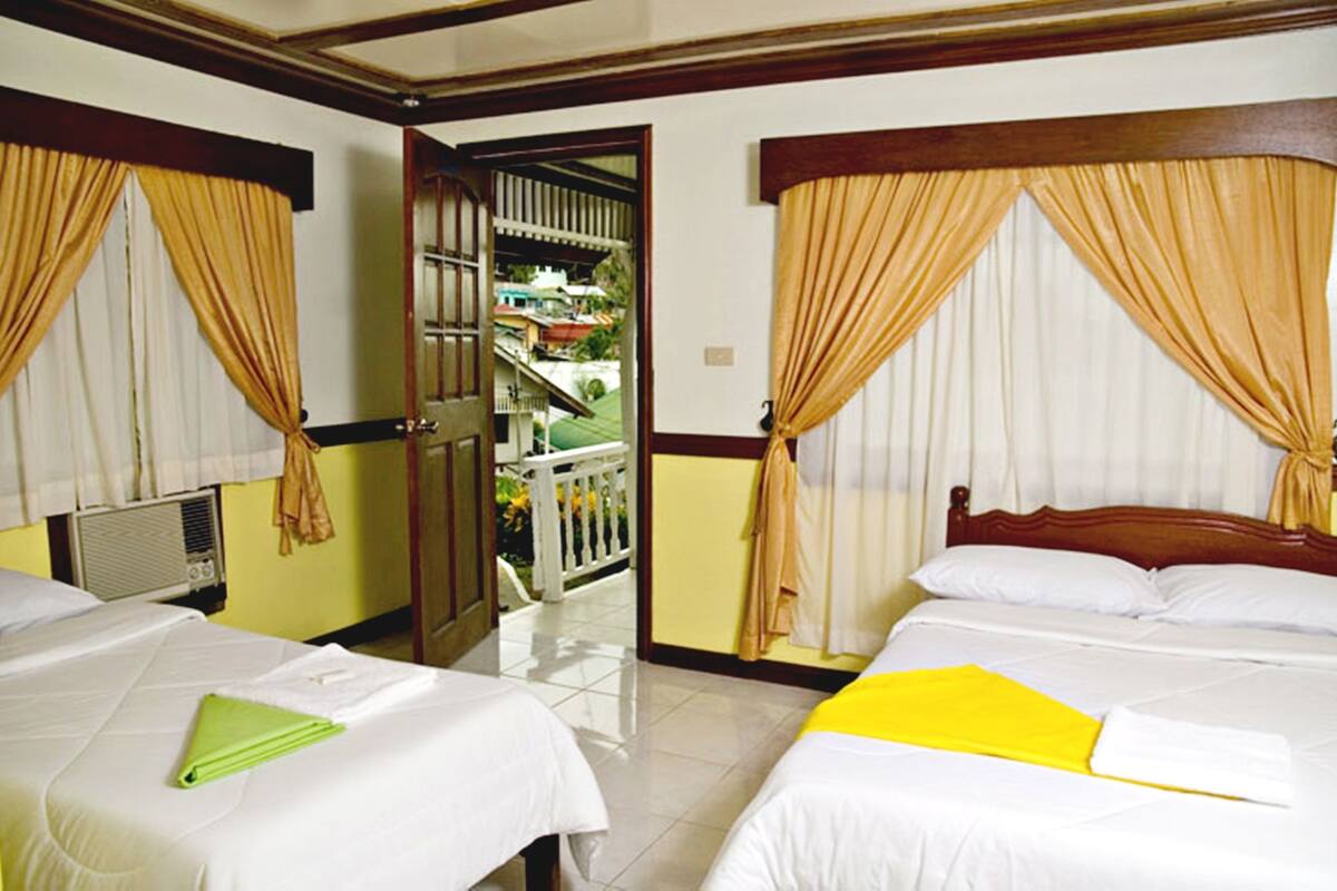A hotel room with two beds, a balcony, and a view of a residential area.