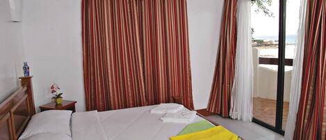 Habitación de hotel con cama, una mesita con una planta, ventana con cortinas y vistas al exterior.