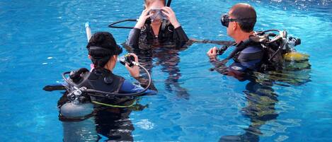 Three people in a swimming pool wearing scuba diving gear.