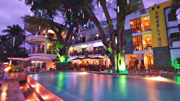 Un hotel con piscina, mobiliario exterior y un edificio de varios pisos con balcones.