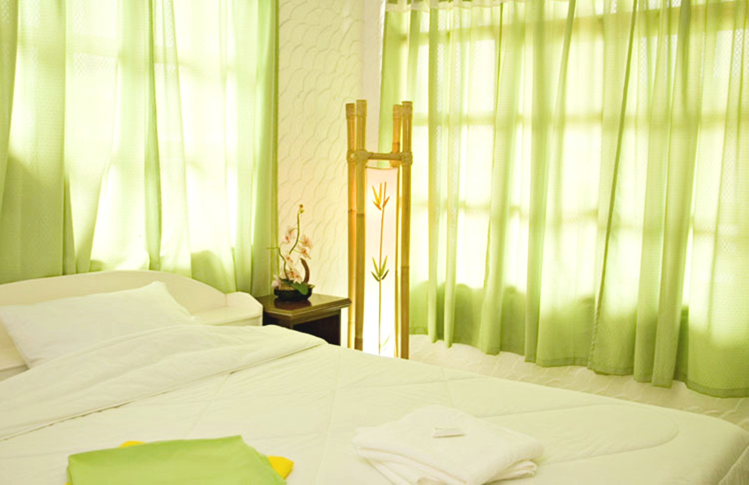 A hotel room with a bed, green curtains, a nightstand with a decorative item, and a wall with a textured pattern.