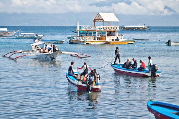 Eine Küstenansicht mit mehreren Booten, darunter ein Hausboot mit einem Reetdach, das in ruhigem Wasser liegt.