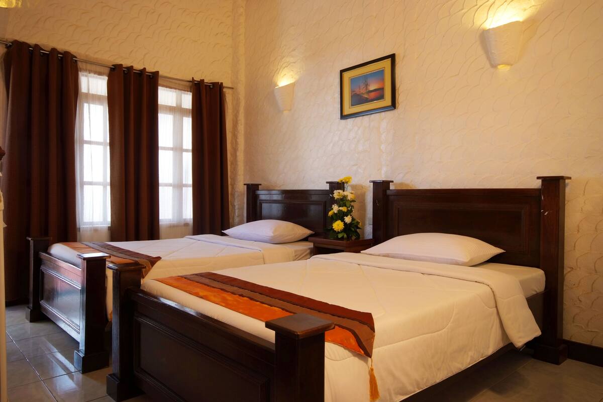 A hotel room with two beds, a wooden headboard, a nightstand with a vase of flowers, and a painting on the wall.