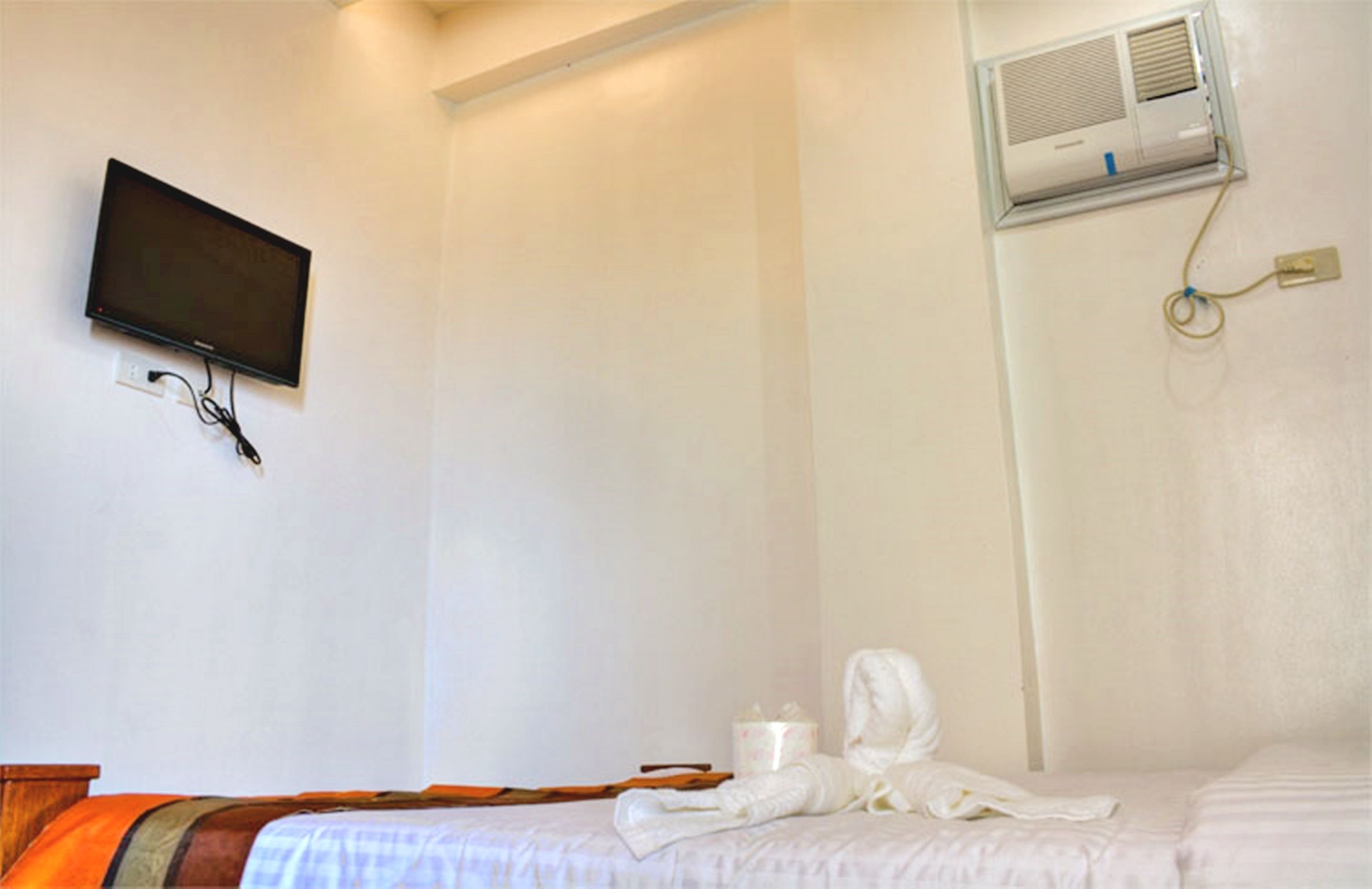 Ein Hotelzimmer mit Bett, einem an der Wand befestigten Flachbildfernseher und einer Klimaanlage.