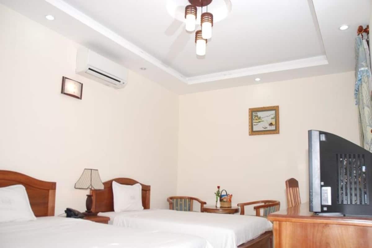 A hotel room with two beds, a desk, a television, and a small table with a lamp.