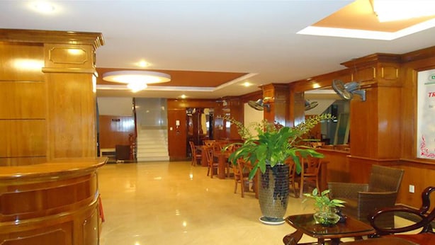 A hotel lobby with a reception desk, a large potted plant, and a staircase leading to other areas. - Phu An Hotel (Ho Chi Minh City)