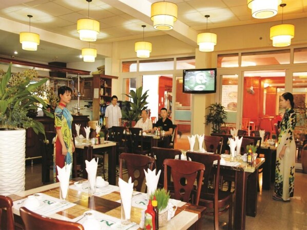 Een restaurant met meerdere eettafels, stoelen en gele hanglampen.