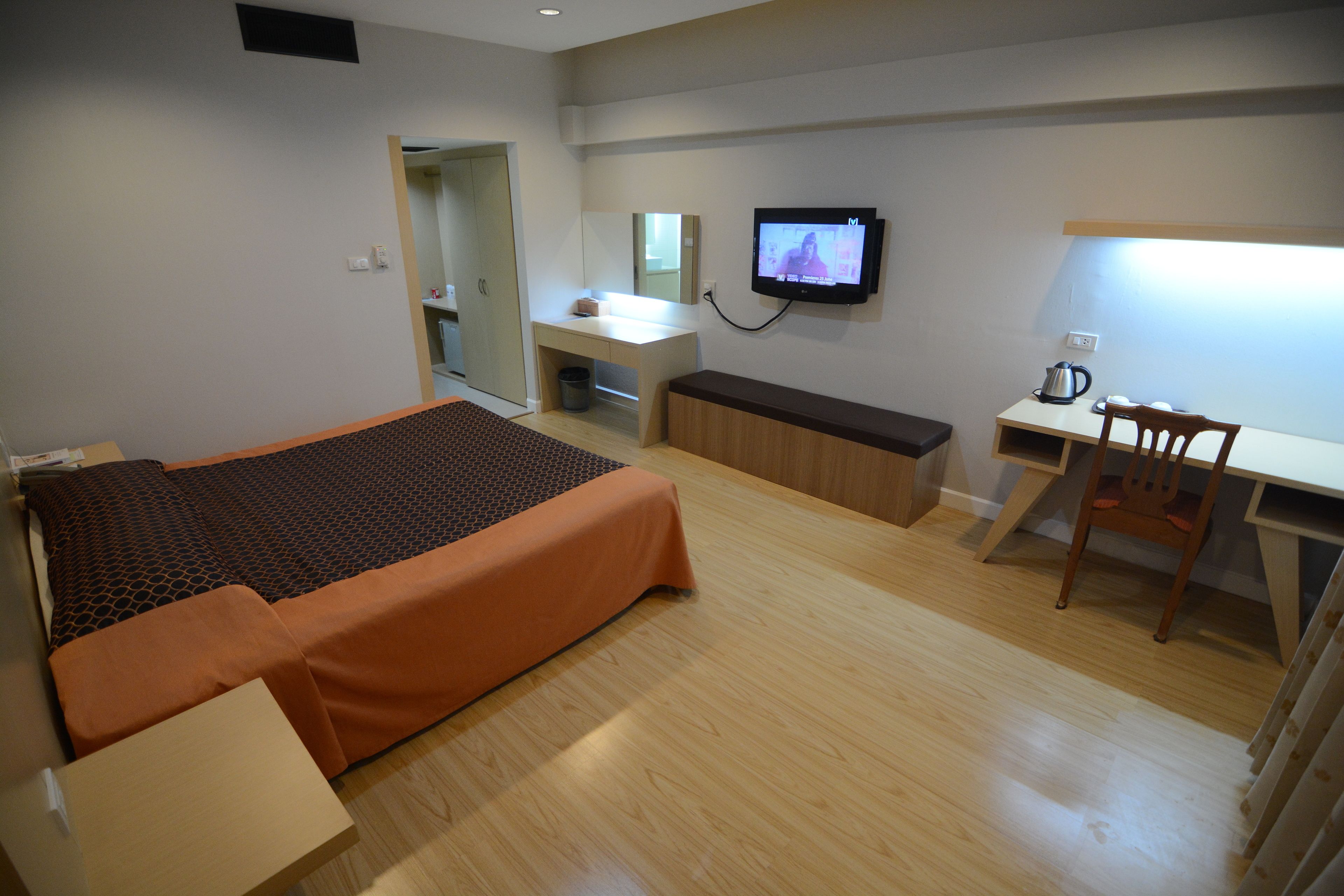 A hotel room with a bed, a desk, a chair, a television, and a small kitchenette.