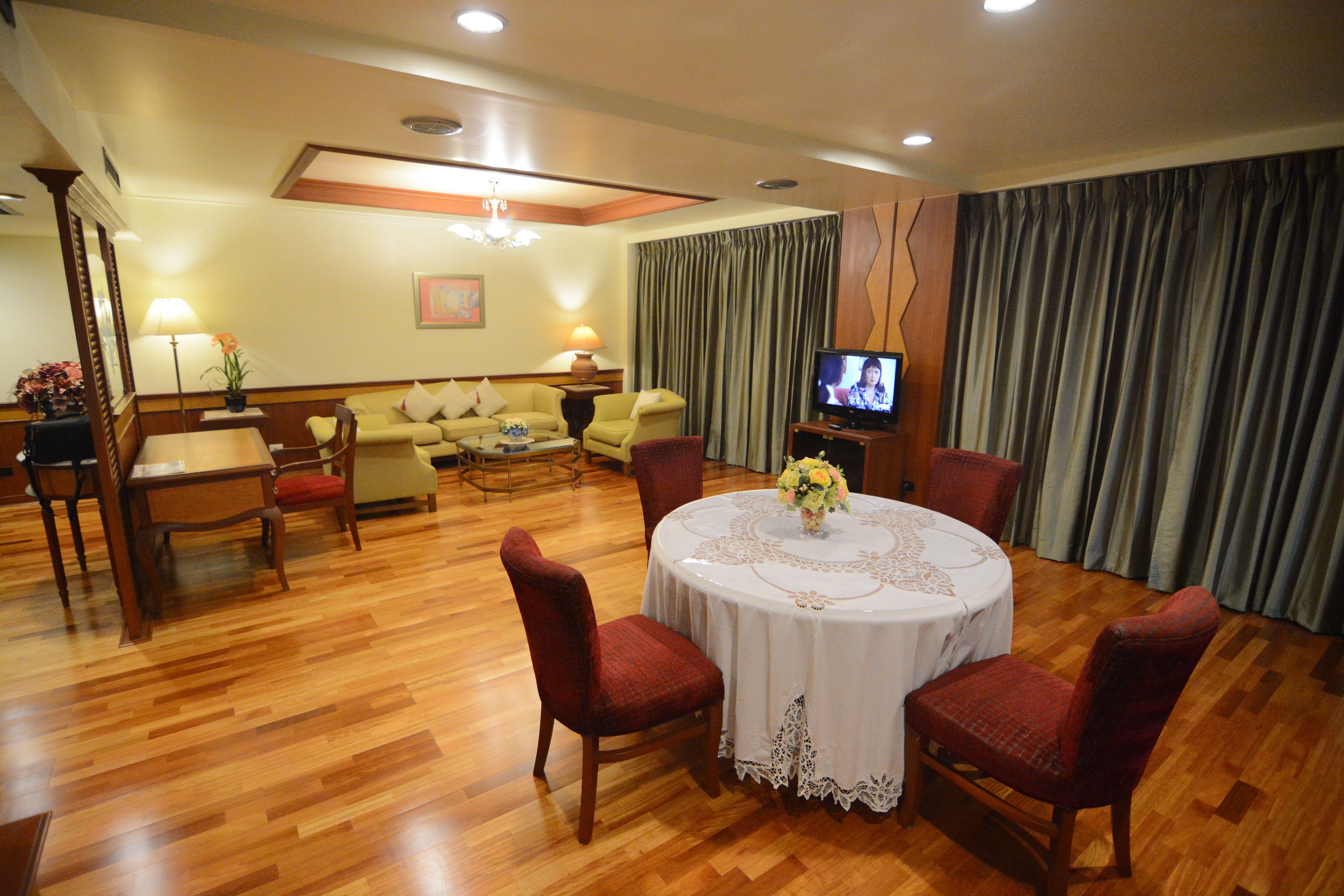 Une chambre d’hôtel comprenant un coin repas, un ensemble de canapés, un téléviseur et un lustre.