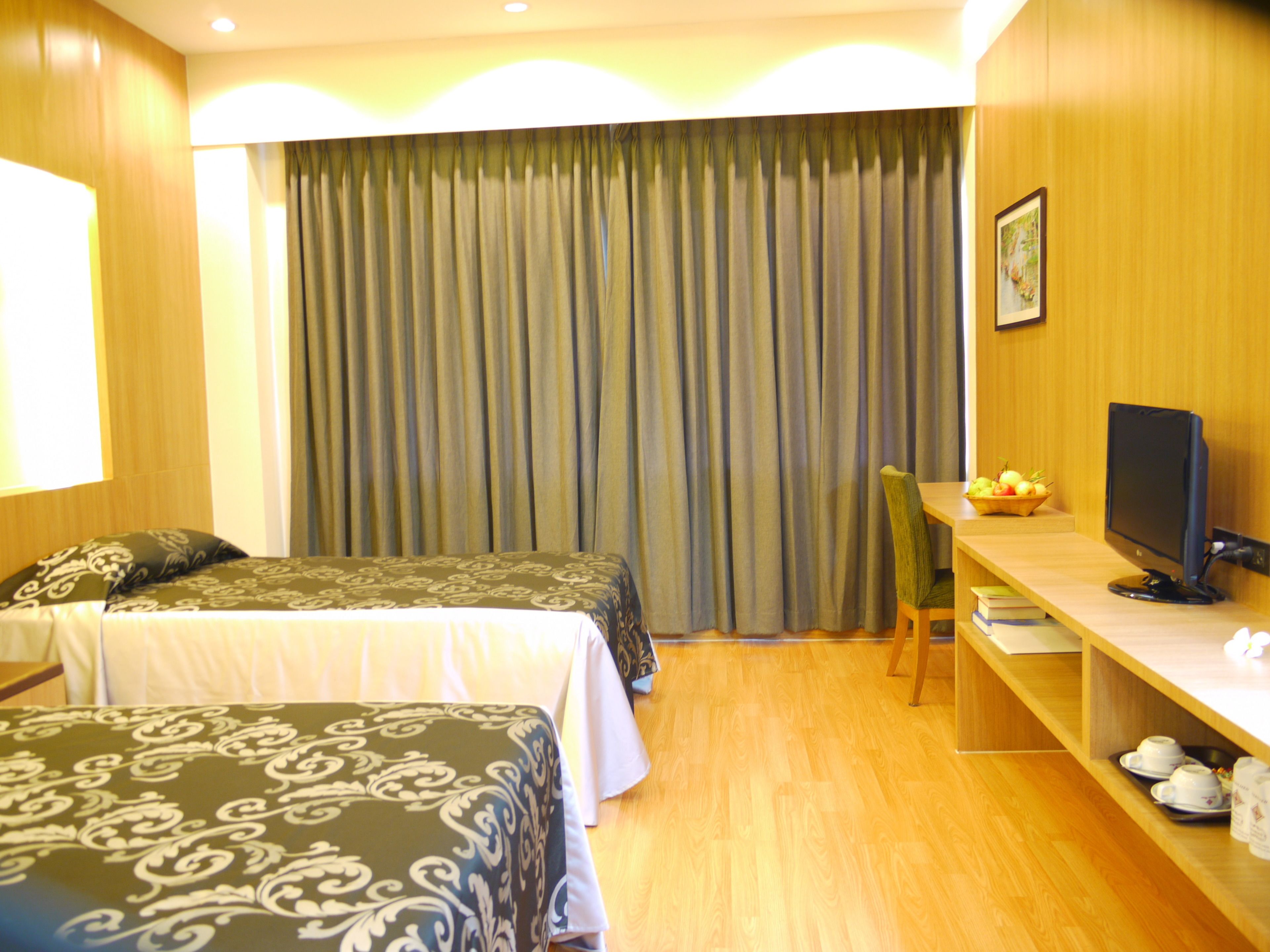 Quarto de hotel com duas camas, uma secretária com computador, uma cadeira e uma mesinha com uma fruteira.