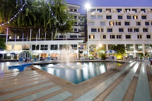 A swimming pool with a fountain, surrounded by outdoor seating and a modern building in the background. - Charoen Hotel (Udon Thani)