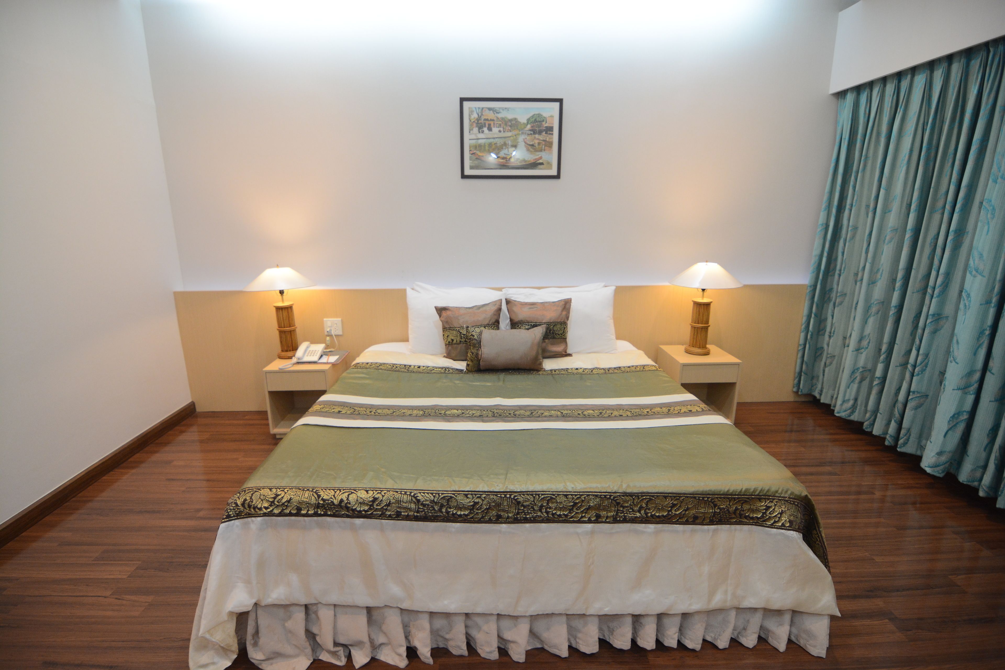 A neatly made bed with a green and white bedspread, two bedside lamps, and a framed picture on the wall.