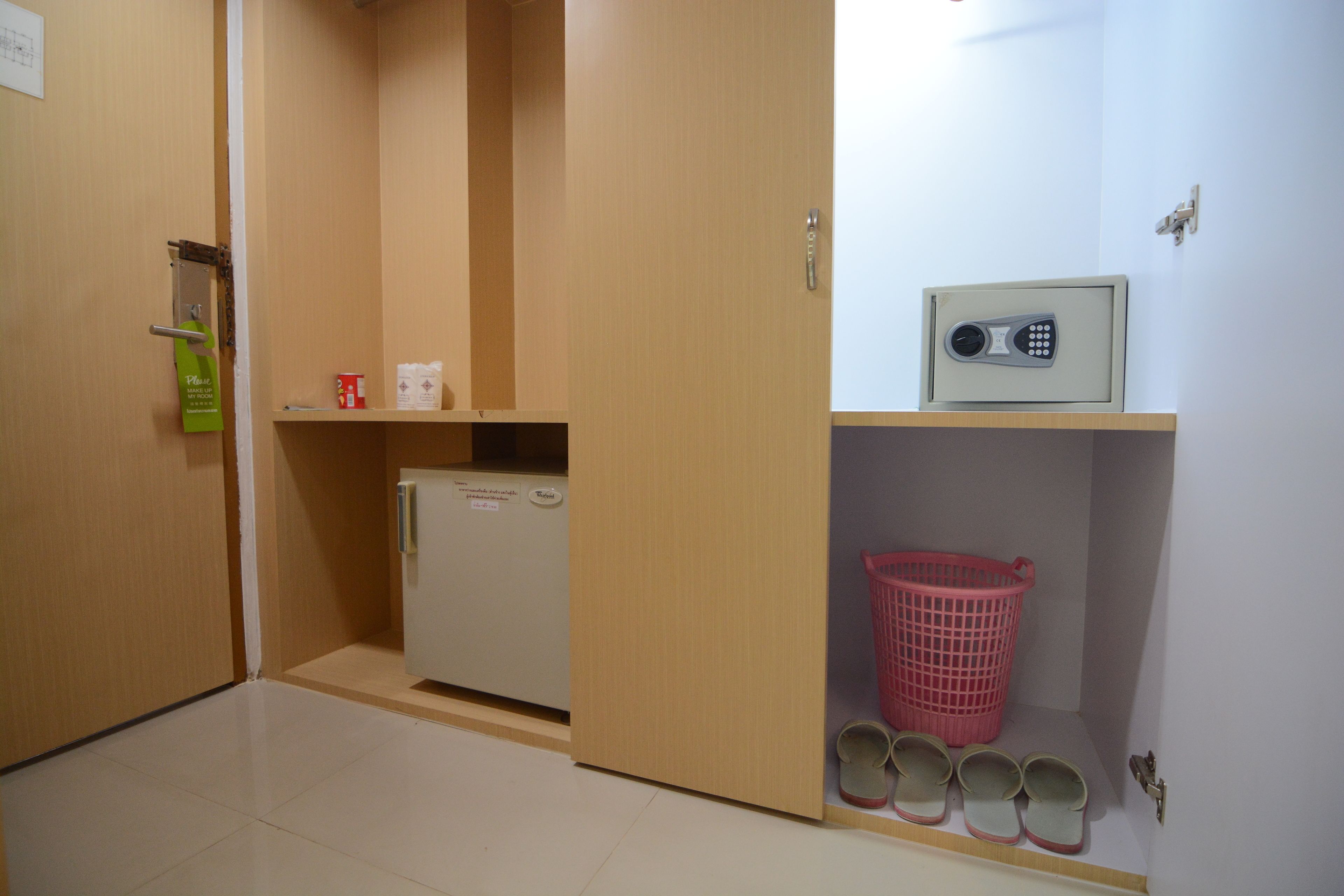A hotel room with a wooden door, a small refrigerator, a pink laundry basket, and a shoe rack.
