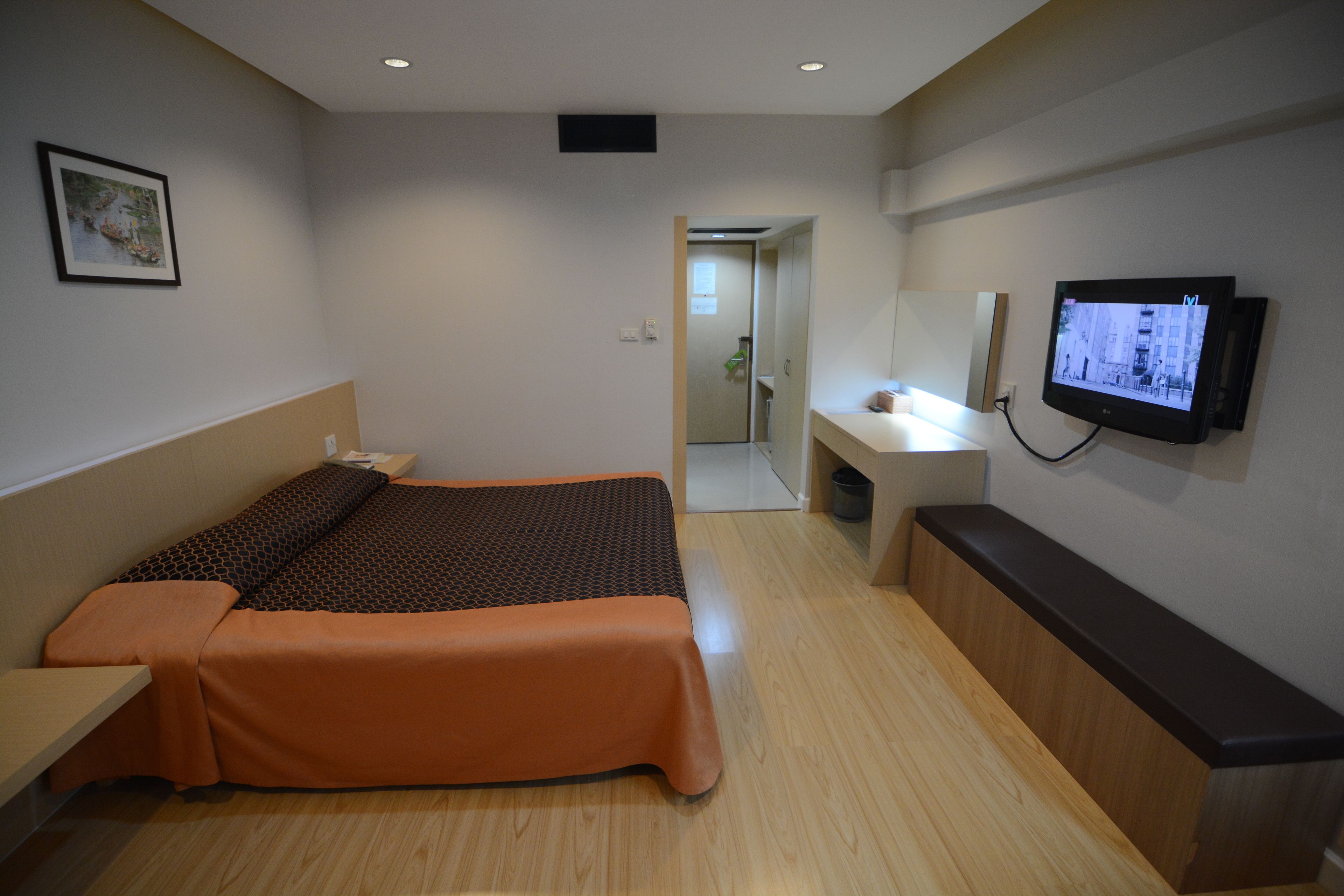 Habitación de hotel con cama, escritorio, televisión y baño visible a través de una puerta abierta.