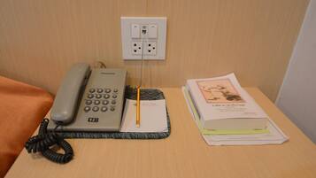 A hotel room with a telephone, a notepad, and some papers on a wooden table.