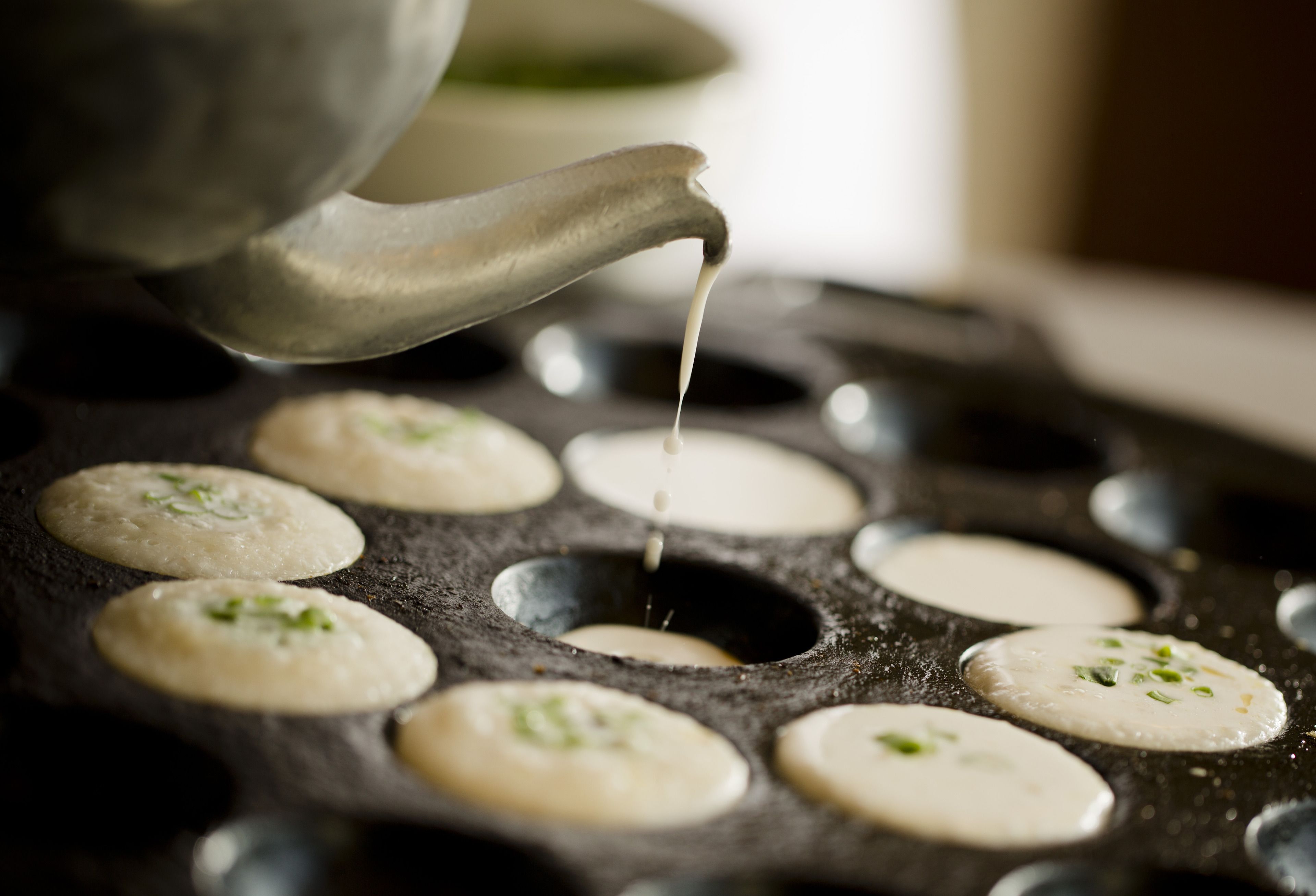 A close-up of a cooking surface with several round molds and a liquid being poured into one of them.