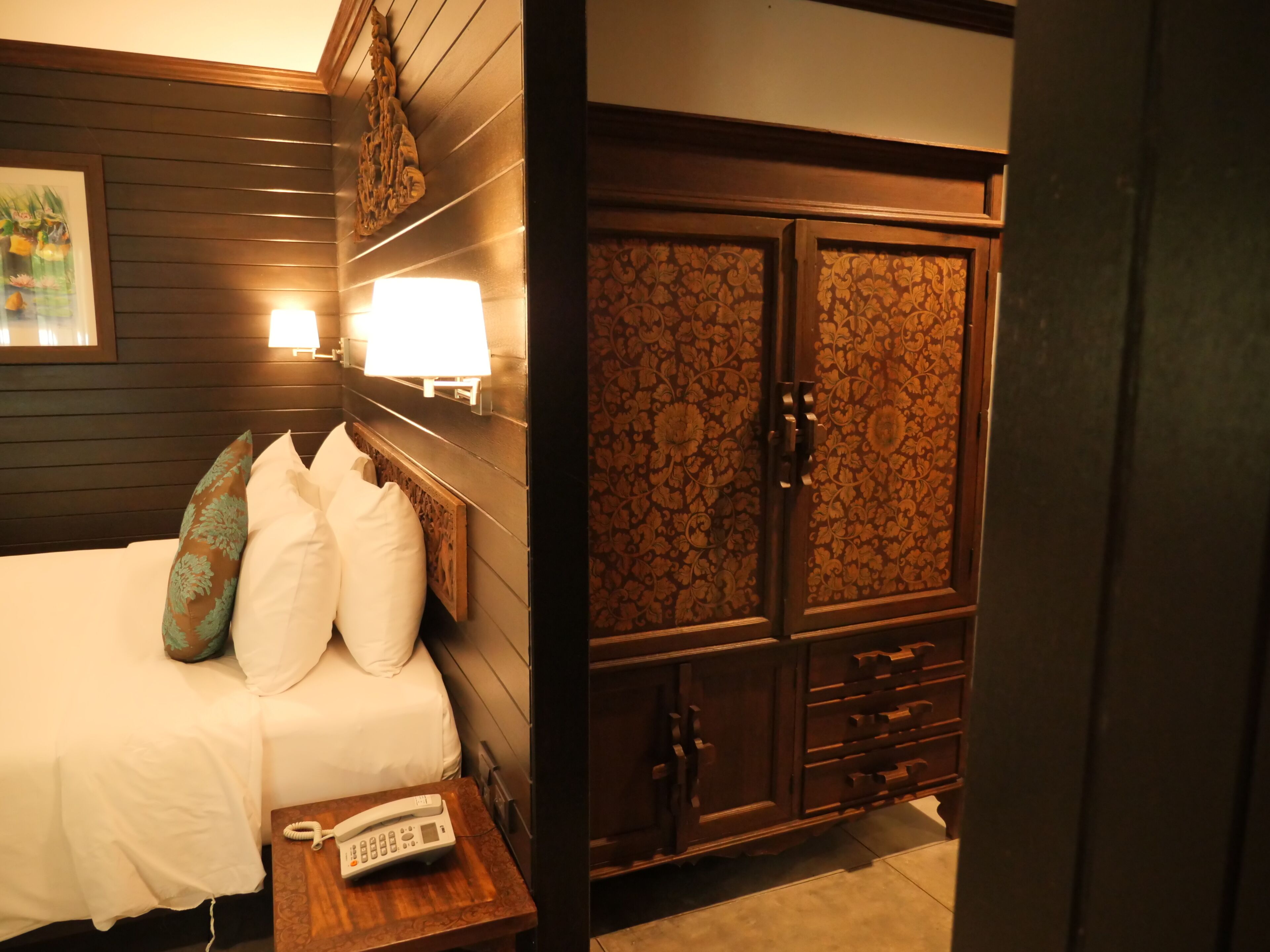 A hotel room with a bed, bedside lamp, telephone, and a wardrobe with intricate patterns.