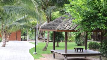 A covered outdoor seating area with benches, surrounded by lush greenery and palm trees.
