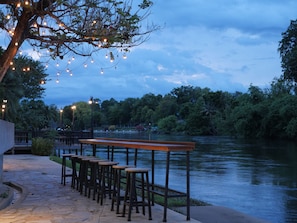 Un bar a la orilla del río con terraza y luces colgantes.