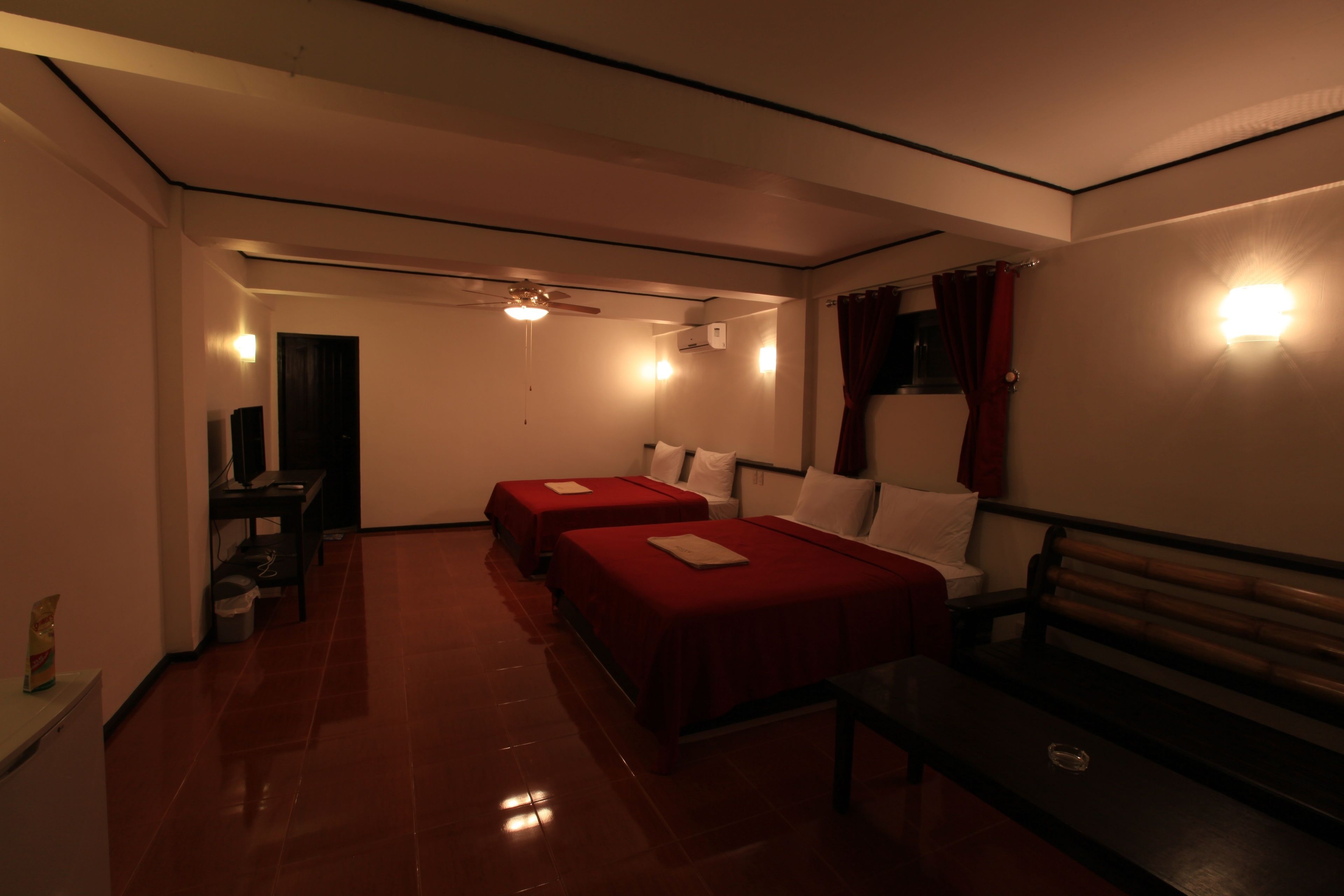 A hotel room with two beds, a bench, a desk, and a ceiling fan.