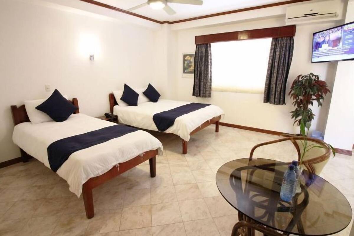 A hotel room with two beds, a glass table, a TV, and a window with curtains.